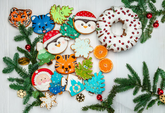 Christmas wreath cake and gingerbread cookies on white background. Flat lay of glazed ring pastry with pomegranate seeds, holiday biscuits, pine twigs, tangerines.