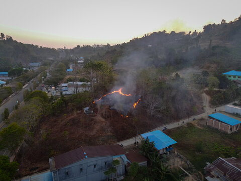 Aerial view of a brush fire burning on a hillside near residential houses and a road in Indonesia.