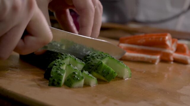 Young woman cuts green cucumber with knife on wooden surface. Fresh vegetable pieces form salad. Daily cooking shows wellness and calm