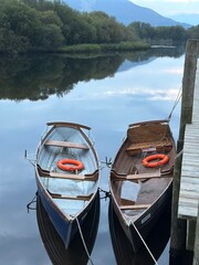     Two traditional wooden rowing boats moored beside a pier on a calm lake, with warm evening light reflected on the water. © olga