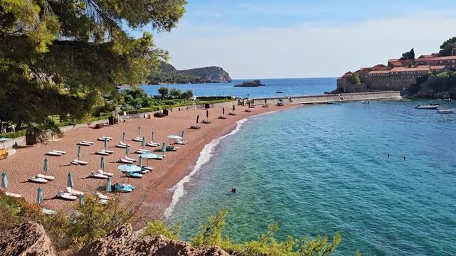 Sveti Stefan beach with sun loungers and turquoise sea in Montenegro