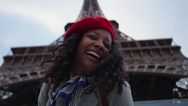 Smiling black woman wearing a red beret playing and looking at the camera while standing in front of Eiffel tower, Paris.