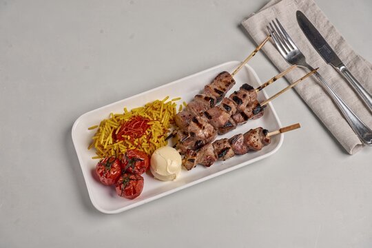 Chelo Kebab with grilled pork skewers, yellow rice, cherry tomatoes, fresh tomato on gray surface. Concept of grilled meat with saffron rice butter for culinary delight.