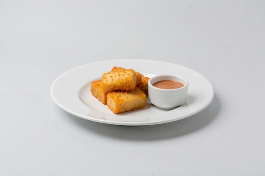 Kibbeling on plate with battered white fish pieces with sauce. Concept of minimalistic presentation, clean lines, and focus on food elements against light grey background.