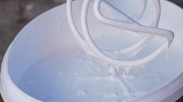 Universal mixer tool spins in bucket of white paint, achieving required consistency for later application on surfaces. This step is essential for even distribution during construction or repair work