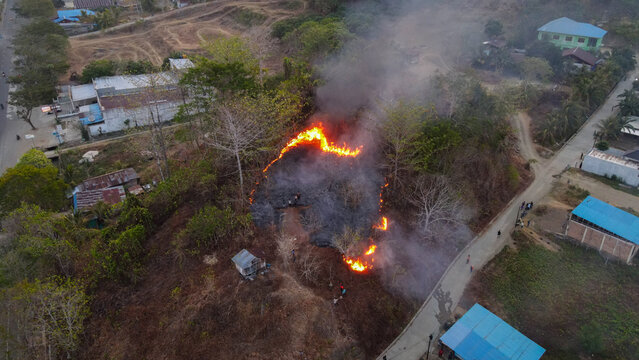Aerial view of a brush fire burning on a hillside near Waisai, with smoke rising above the landscape and nearby buildings in Raja Ampat, Southwest Papua, Indonesia.