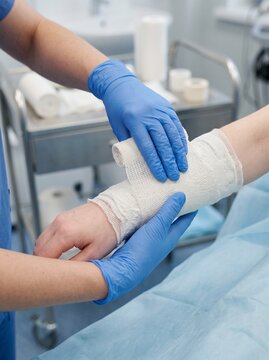 commercial medical stock photograph, 45-degree close-up of orthopedic healthcare professional hands applying a clean plaster cast around a patient's lower arm, modern orthopedic clinic