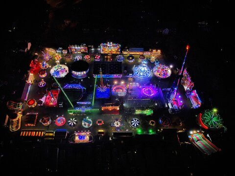 Aerial view of the illuminated funfair at Spencer Park with colorful spinning rides, bright neon lights, and carnival attractions at night in Rushden, England, United Kingdom.