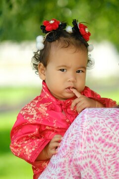 Adorable Asian baby girl in traditional red silk dress outdoors wearing cute hair accessory