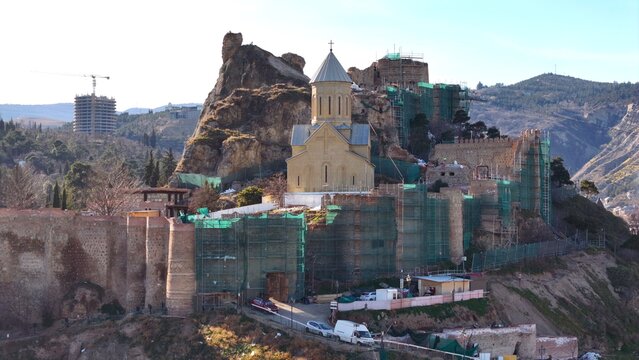 Aerial view of Narikala Fortress and St. Nicholas Church surrounded by historic stone walls and scaffolding on a hillside in Tbilisi, Georgia.