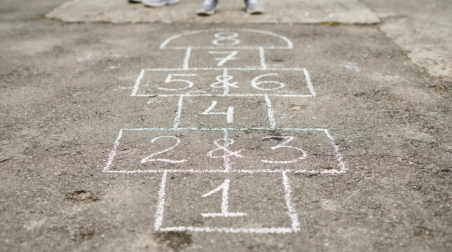 Hopscotch game drawn with chalk on pavement, children playing and jumping on numbered squares. Hopscotch gameplay involves physical activity and counting numbers,