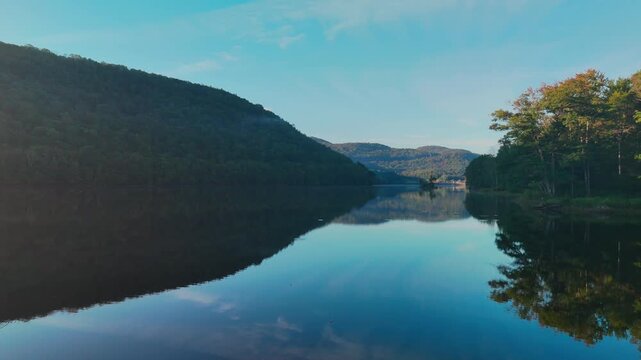 Calm water view at Sherman Reservoir Boat Launch, Vermont, USA, with forested mountains, tree reflections and clear sky, representing peaceful nature and boating recreation. 4K.