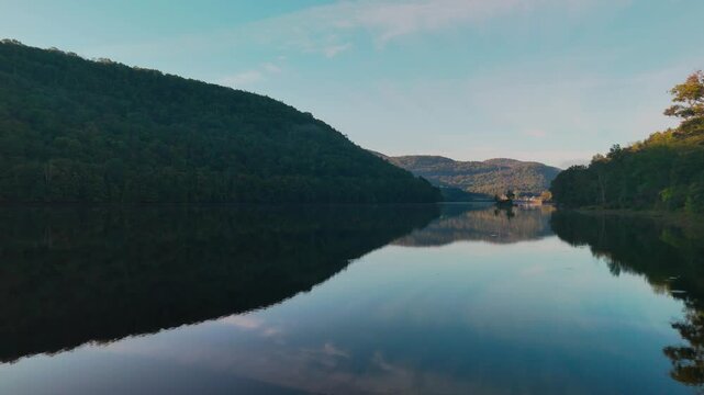 Calm water view at Sherman Reservoir Boat Launch, Vermont, USA, with forested mountains, tree reflections and clear sky. Sunny weather. Peaceful nature and boating recreation. 4K.