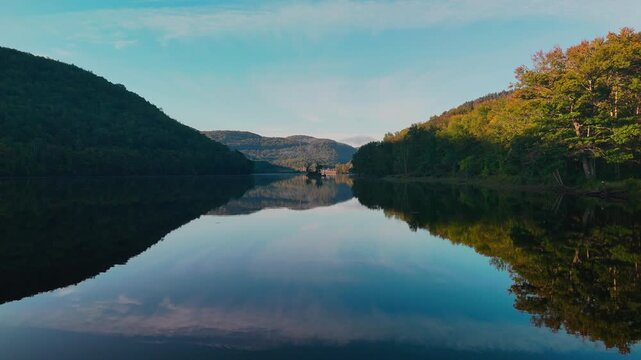 Scenic calm water drone view at Sherman Reservoir Boat Launch, Vermont, USA, with forested mountains, tree reflections and clear sky. Peaceful nature and boating recreation. 4K. Slow dolly.