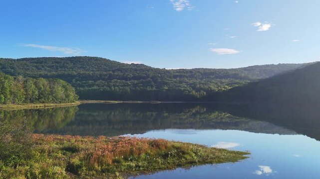 Scenic water drone view at Sherman Reservoir Boat Launch, Vermont, USA, with forested mountains, tree reflections and clear sky. Peaceful nature and boating recreation. 4K.