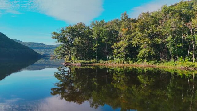 Serene lake reflecting forested mountains under blue sky, representing tranquility, wilderness, travel, and natural scenic beauty. Sherman Reservoir Boat Launch, Vermont, USA.