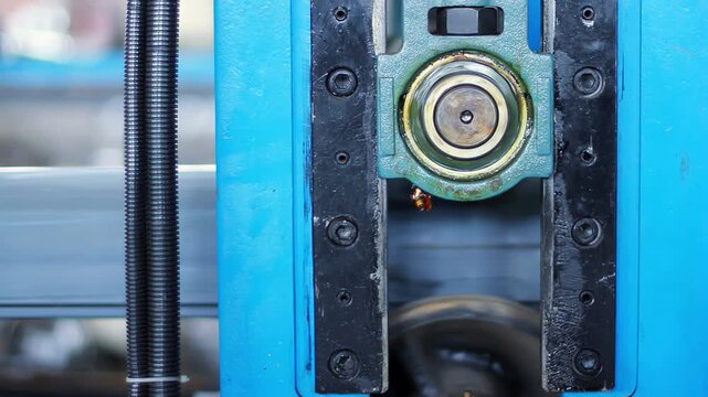 Bearing unit close up blue machine frame. Grease drop metal pipe factory line.