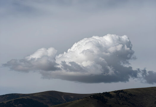 Weather forecast and climate change, single white cumulus cloud floating over rolling hills in a moody overcast sky during a transition of seasons