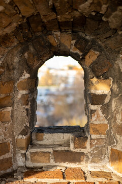 brick arch window in ancient fortress wall close-up, view through stone loophole of historical castle with blurred background, vertical shot of old brick embrasure in medieval fortress