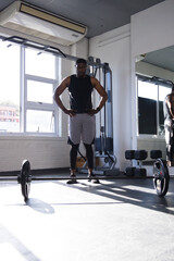 Fototapeta premium African man standing hands on hips facing barbell in gym wearing black sleeveless top, gray shorts