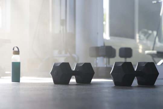 Pair of black hex dumbbells are resting on dark rubber gym floor near green water bottle