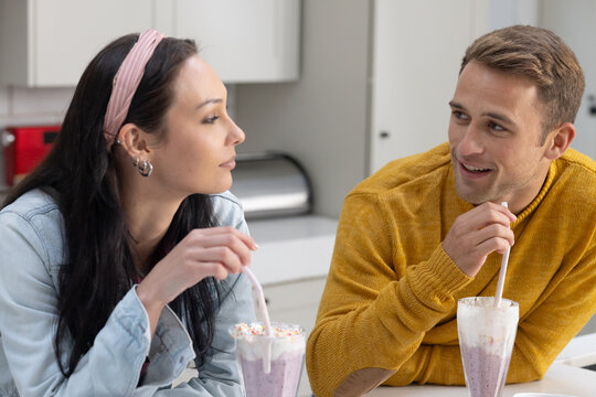 Couple sitting at counter sipping shakes with straws, woman headband, man yellow sweater, toaster