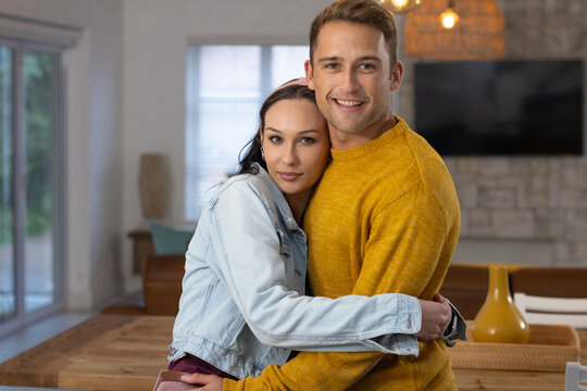 Couple standing centered in living area, leaning together, showing wooden table and yellow vase