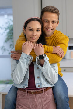Adult couple with male sitting on counter hugging female in kitchen wearing denim and smartwatch