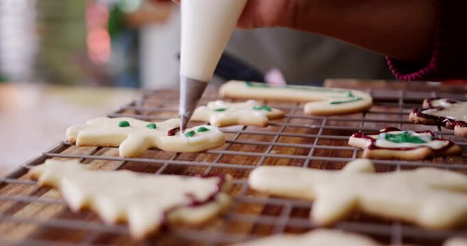 Female bakers piping icing on cooling rack cookies at home, nozzle entering frame preparing treats