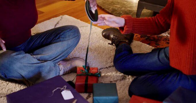 Two women unspooling ribbon with spool appearing, tying bow on box for gifts at home