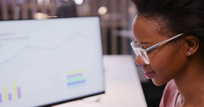 Adult African woman tracking desk monitor leaning analyzing chart in specs and pink top, copy space