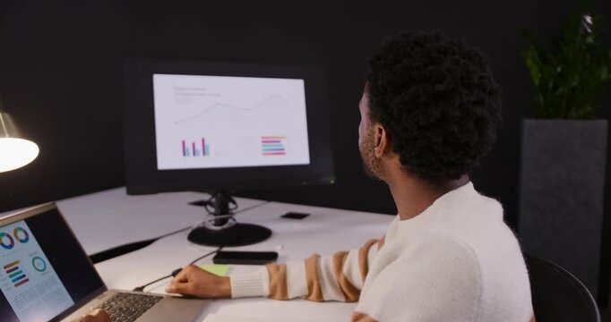 African American man turning to external monitor with charts, checking, updating laptop, copy space