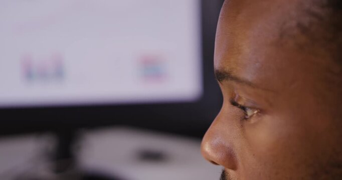 African man in 20s scanning monitor charts, analyzing data and furrowing brow in office, copy space