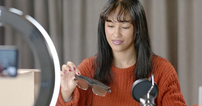 Female pulling sunglasses from pouch, inspecting lenses, showing to phone in studio for review