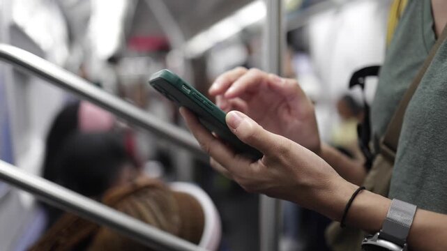 Woman's hands texting on a smartphone while commuting on a crowded new york city subway train, showing a typical urban lifestyle and modern communication habits