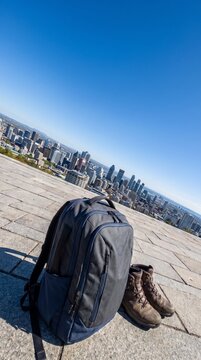 Backpack and hiking boots on a stone terrace overlooking a city skyline. Dutch tilt wide angle perspective of urban travel and adventure concept