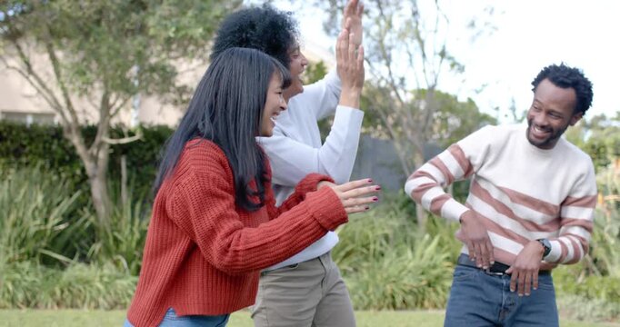 Diverse friends starting by raising hands, playing and dancing in backyard wearing red sweater