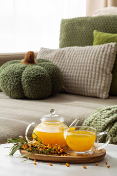 Cozy autumn scene with a glass teapot and cup of sea buckthorn tea and fresh berries on a tray