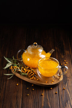 Warm sea buckthorn tea in glass teapot and cup with fresh berries on wooden background