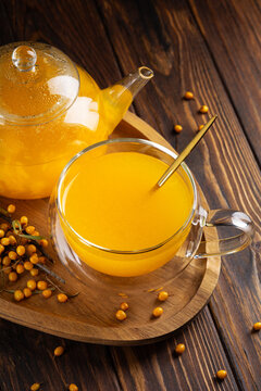 Delicious orange sea buckthorn juice served in clear glass cup with fresh berries and teapot