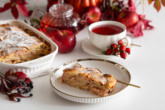 Warm apple cake slice served with hot tea in a white porcelain cup and saucer