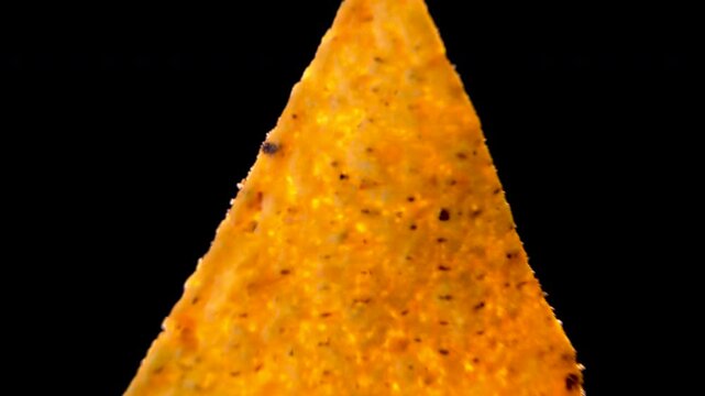 Extreme macro of triangular corn nacho chip with dark seasoning spots on black background