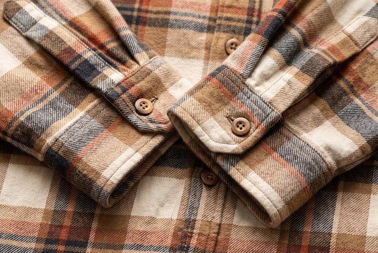 Close up of soft brown plaid flannel shirt with folded sleeves and wooden buttons, representing cozy seasonal autumn and winter fashion and casual rustic style.