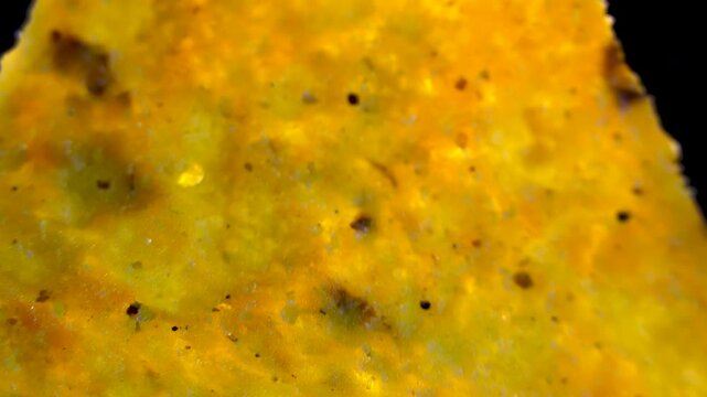 Macro view of triangular corn nacho chip with spices rotating on black background