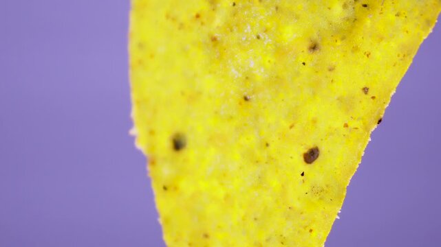 Triangular corn nacho chip with salt crystals rotating on purple background, macro