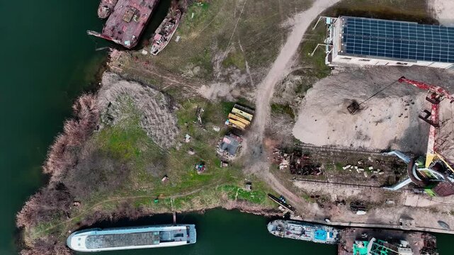 Moored river vessels and floating crane in an industrial harbor, viewed by drone from above. Inland water transport, river-port infrastructure and waterfront layout