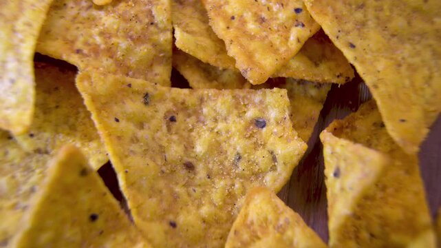 Triangular corn nacho chips with seasoning rotating in a pile, macro close-up