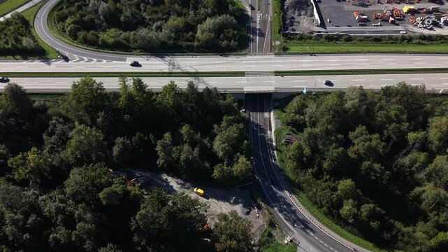 Aerial drone view of vehicles traveling along a road beneath a highway, with additional traffic visible on the elevated motorway.