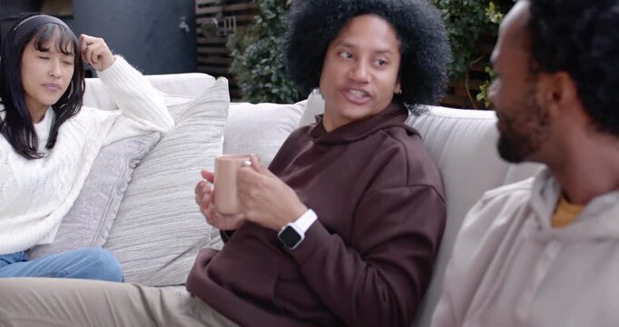 Diverse friends sitting on patio sectional, brown-hoodie speaker holding beige mug, starting story
