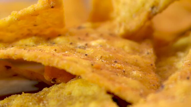 Extreme macro of crispy corn nacho chip surface with dark spices rotating